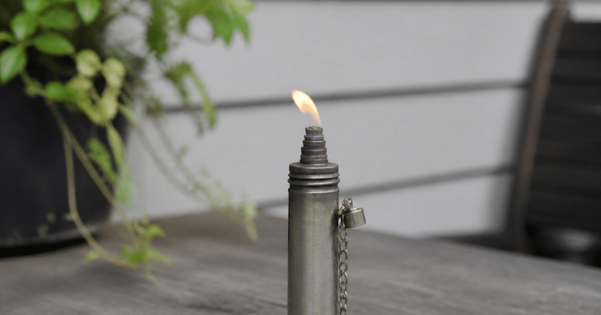 Petit cylindre metallique vertical avec flamme orange faible sortant du bec