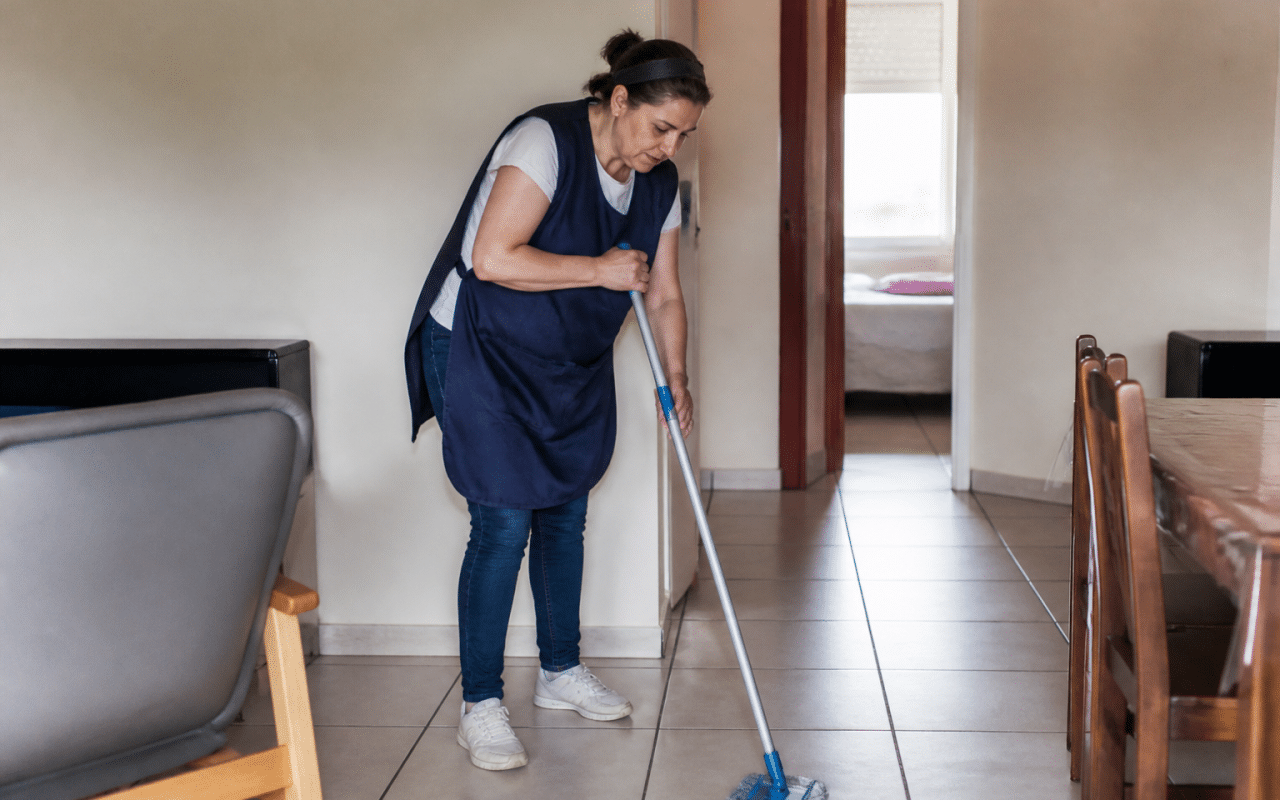 Femme en tablier nettoyant sol avec balai et serpillière