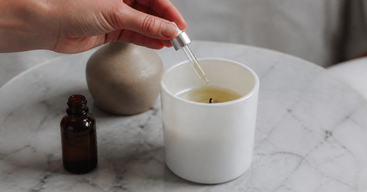 Main versant huile parfumée dans bougie blanche fondue