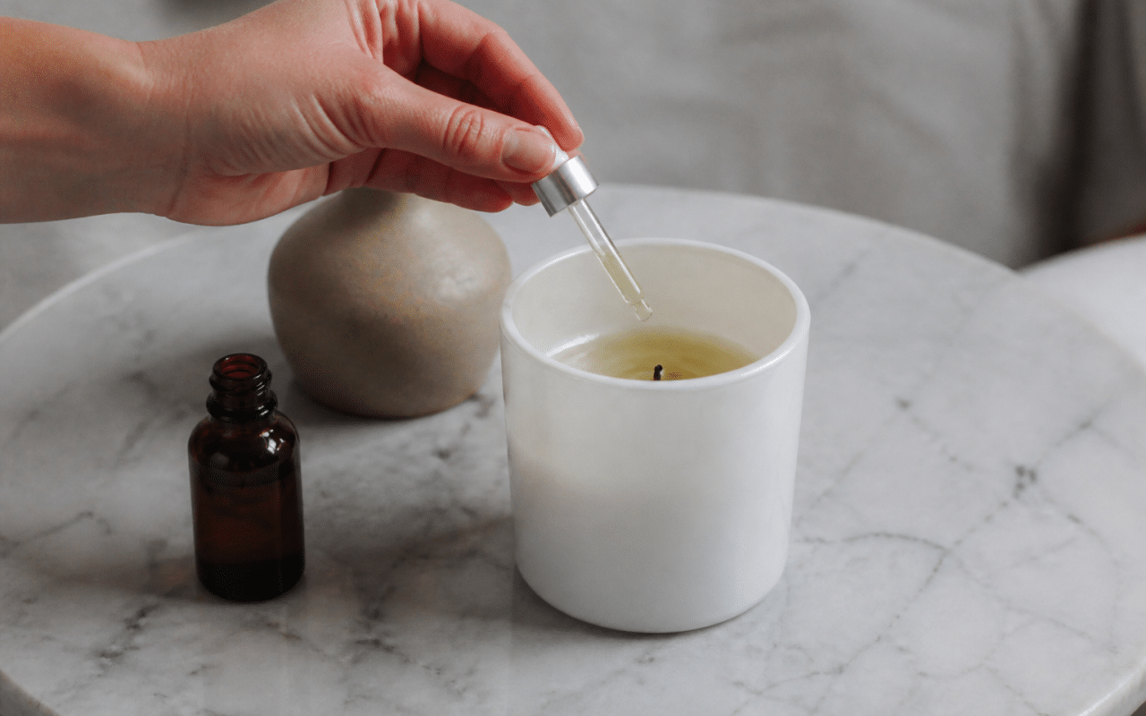 Main versant huile parfumée dans bougie blanche fondue