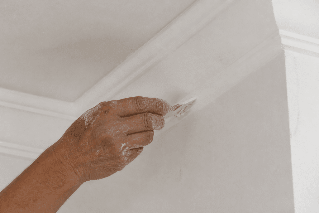 Mains appliquant mastic blanc sur jonction corniche murale
