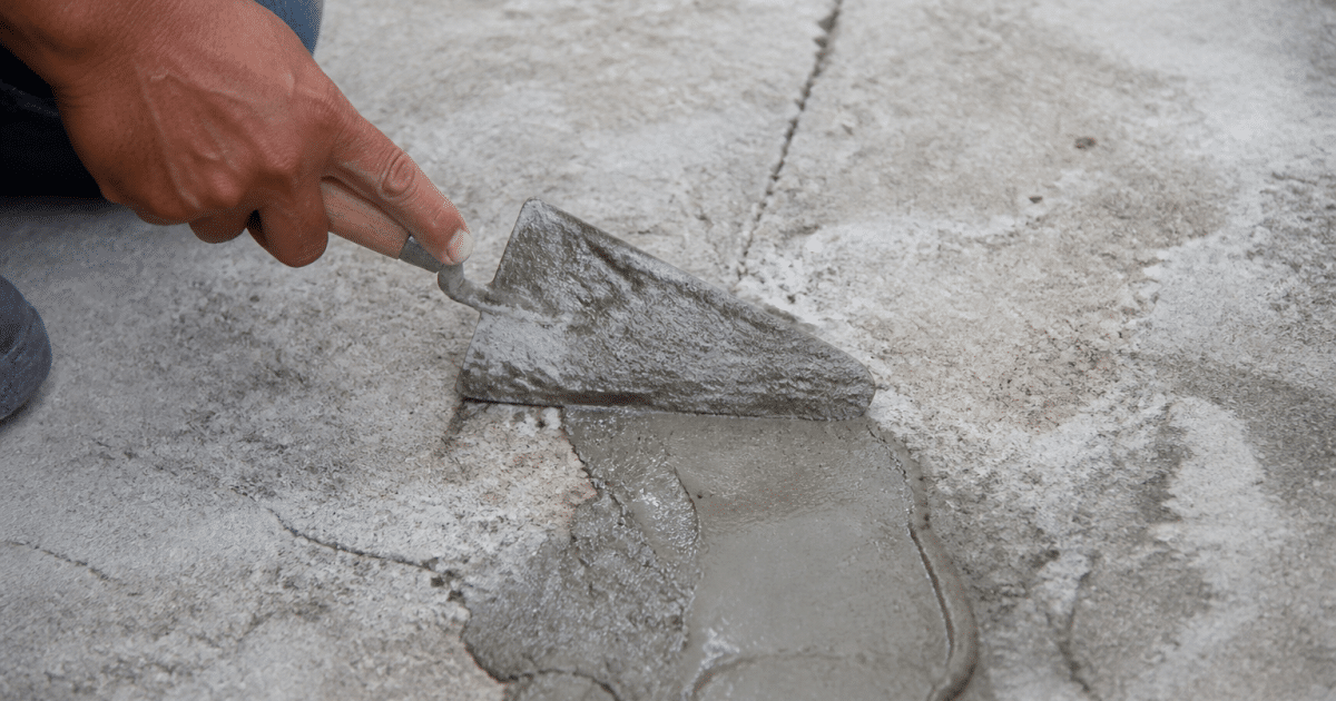 Truelle appliquant mortier gris sur surface beton fissuree