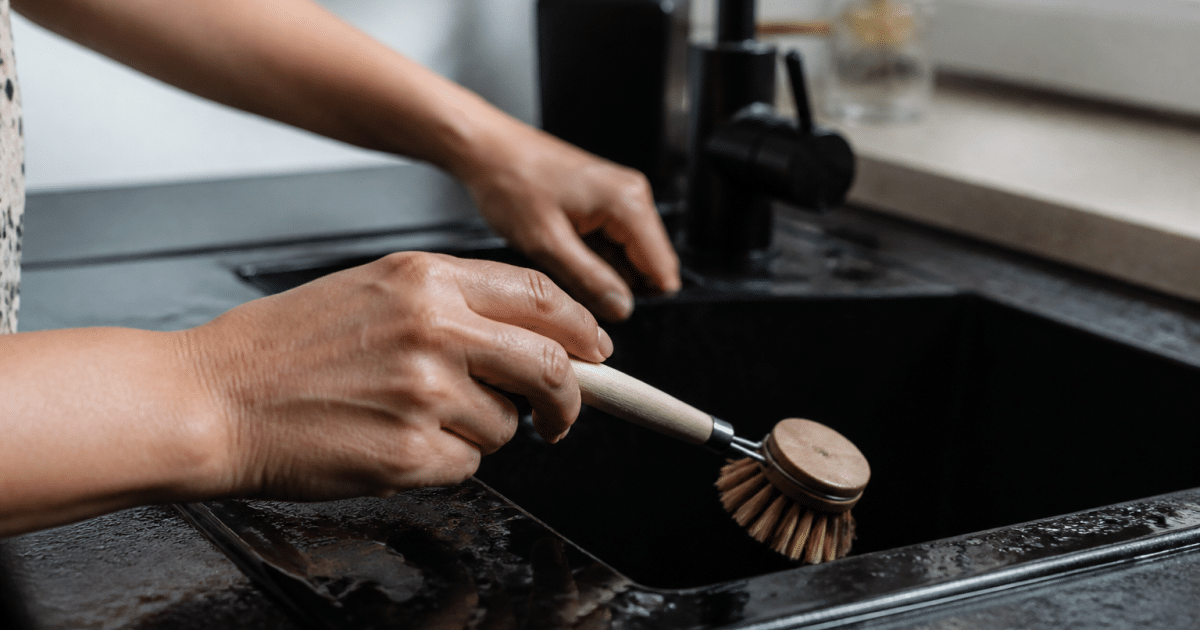 Mains tenant une brosse sur evier noir brillant
