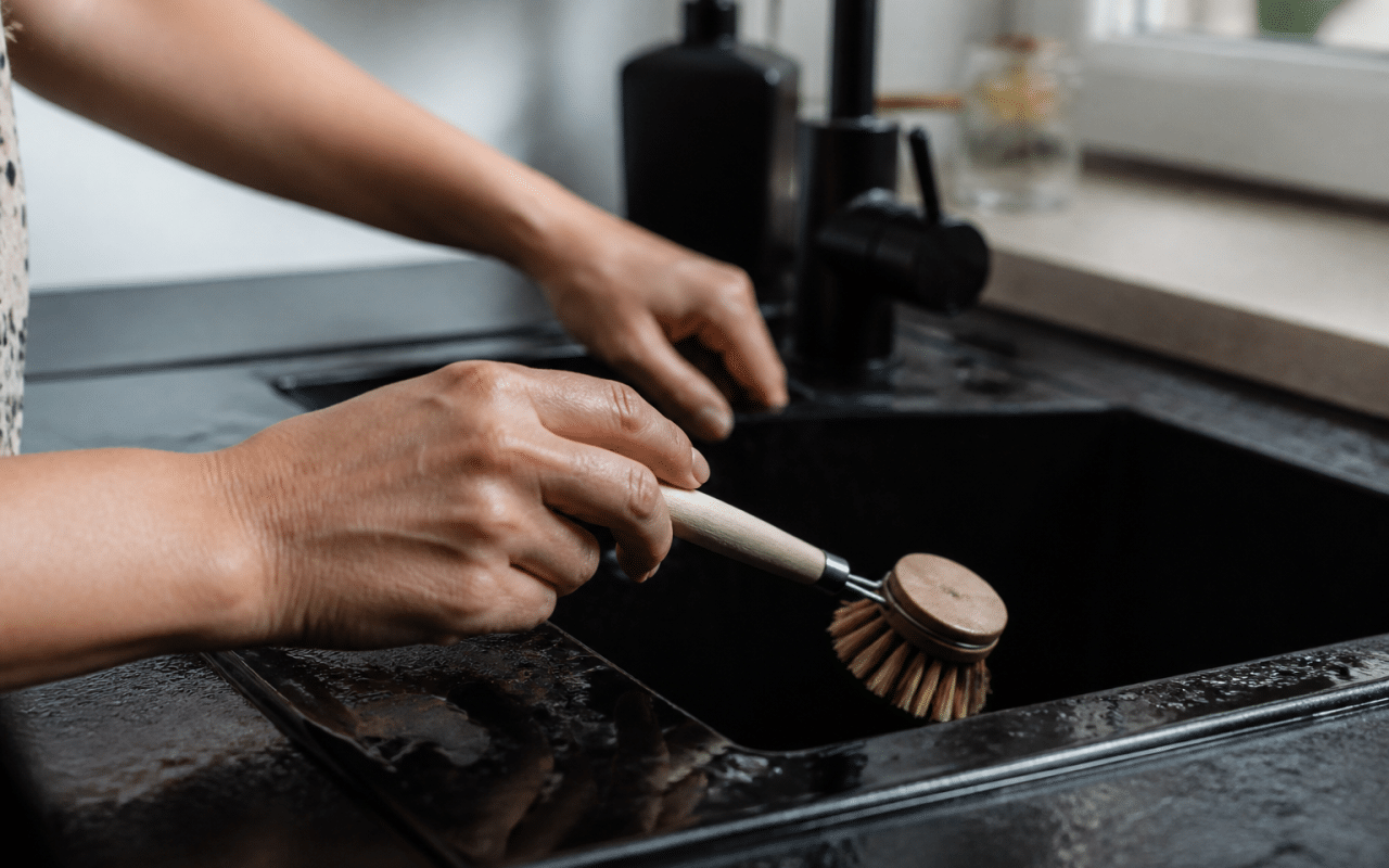 Mains tenant une brosse sur evier noir brillant