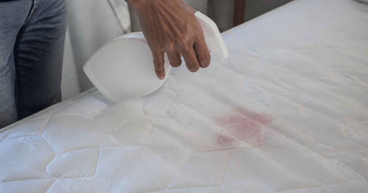 Main appliquant produit nettoyant sur tache rouge matelas blanc