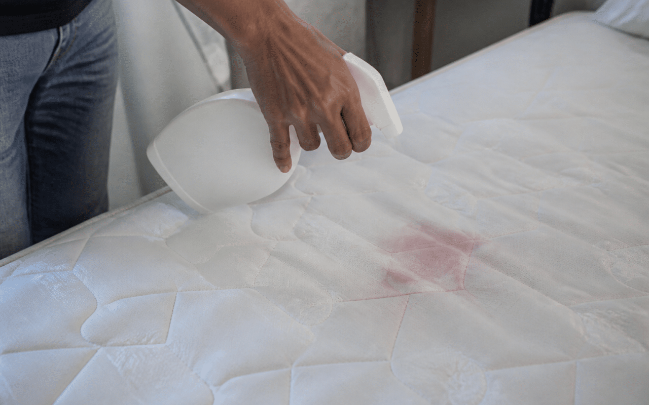 Main appliquant produit nettoyant sur tache rouge matelas blanc